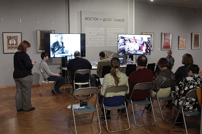 Люди в зале наблюдают за онлайн встречей в России