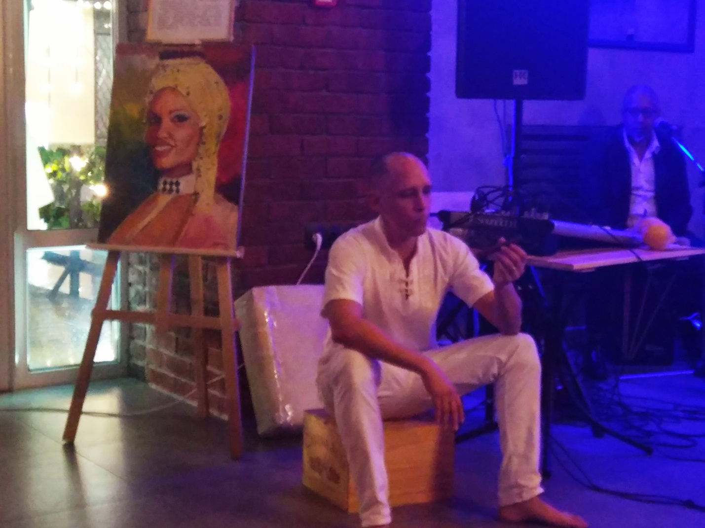 Мужчина сидит на стуле, а взади него картина с кубинской женщиной