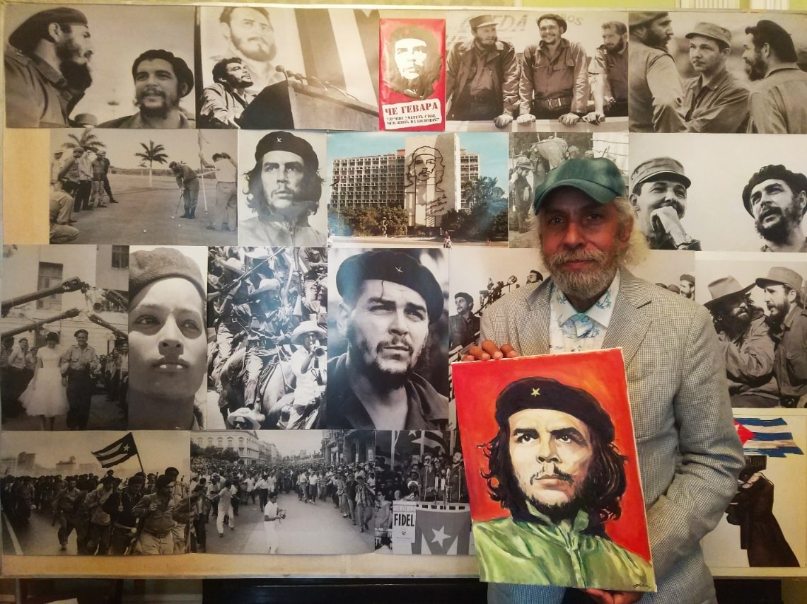 На фото Кубинский художник Омар Годинес с портретом Эрнесто Че Гевары в руках выполненный на красном фоне, а позади Омара стенд с фотографиями Эрнесто Че Гевары