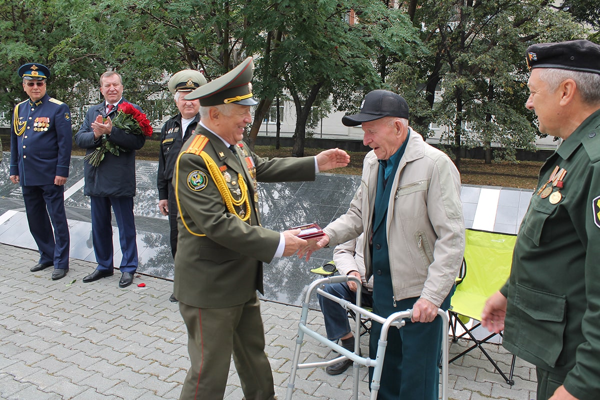 Мужчина в военной форме вручает ветерану медаль
