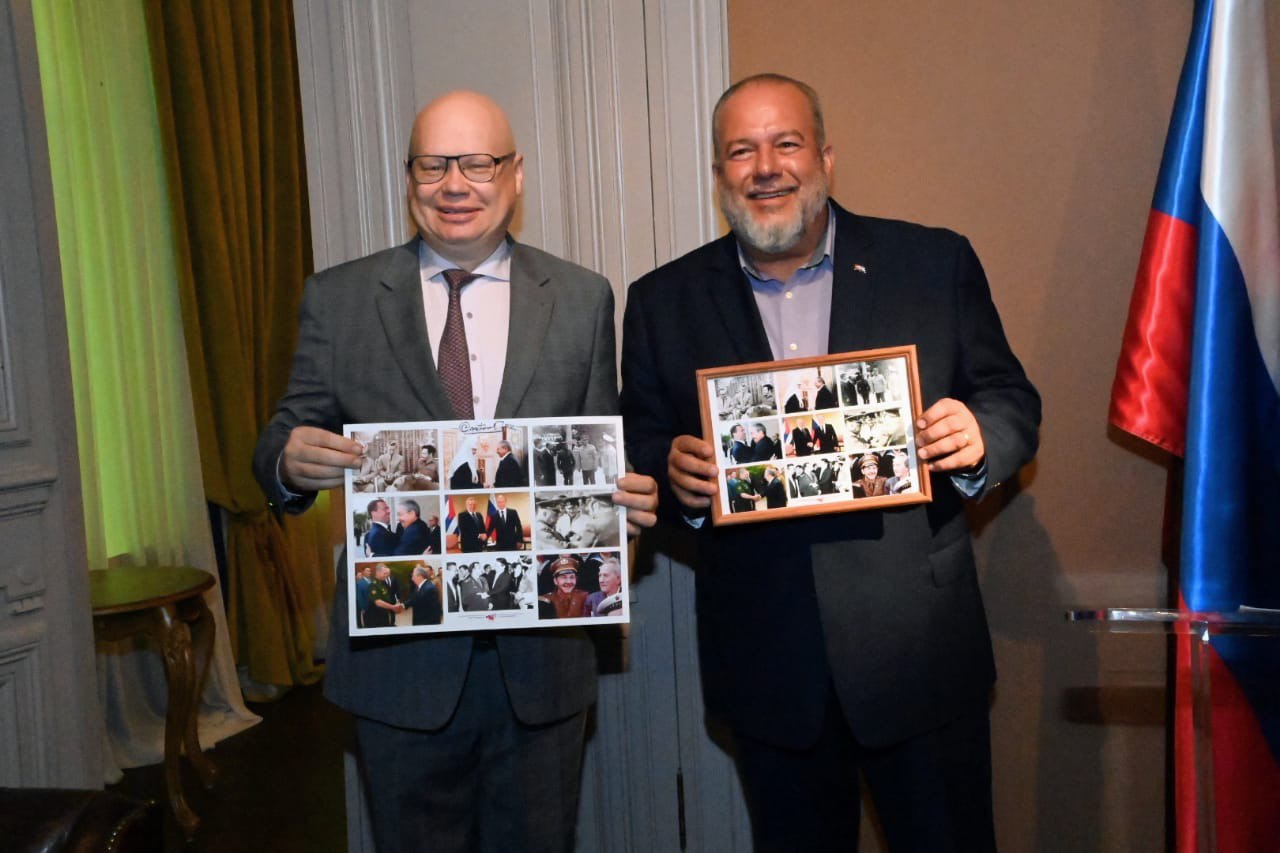 Мануэль Марерро Крус и Алексей Михайлович Лавров стоят с рамками в которых фотографии со встреч выскопоставленных лиц России и Кубы